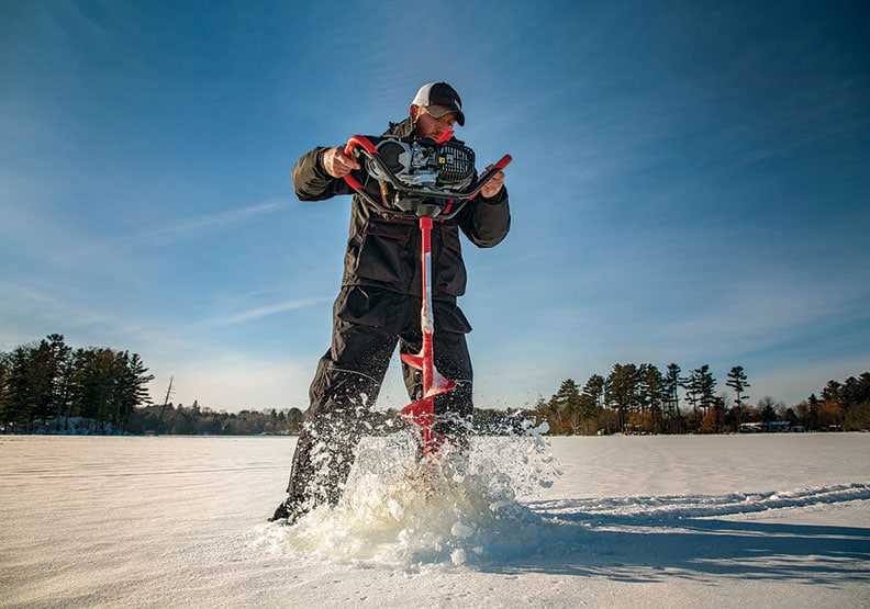 Man using a powered ice auger to make a hole in the ice