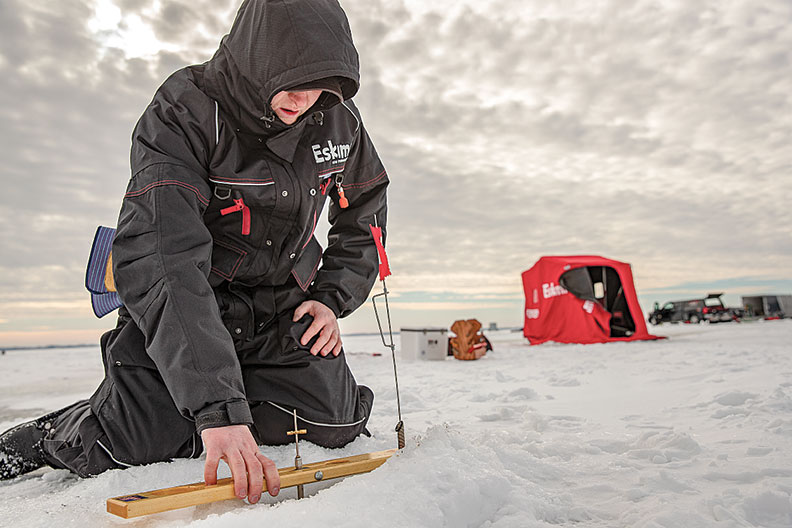 Man on frozen lake making preparations for ice fishing.