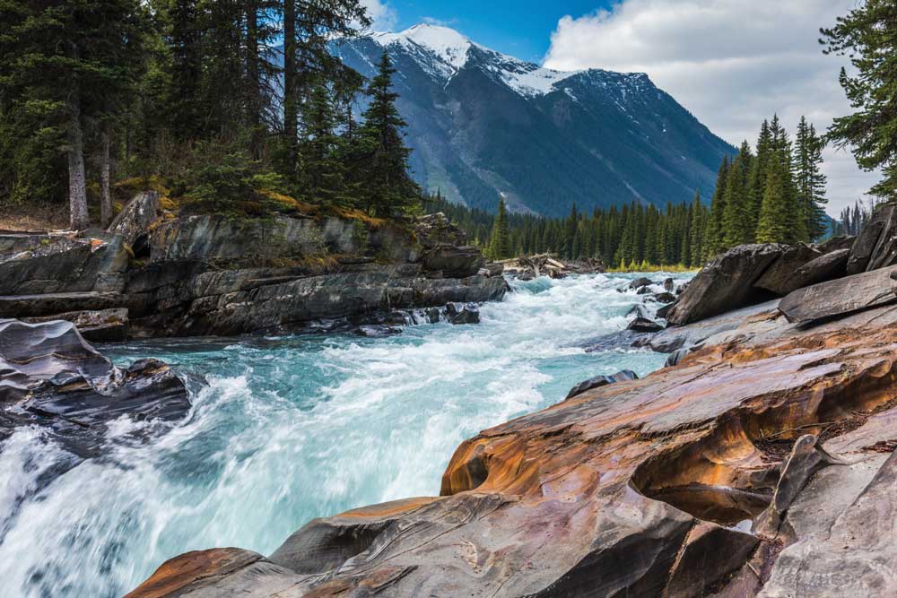 Rocky shoreline and rushing water of Kootenay cascade Numa Falls off BC Highway 93