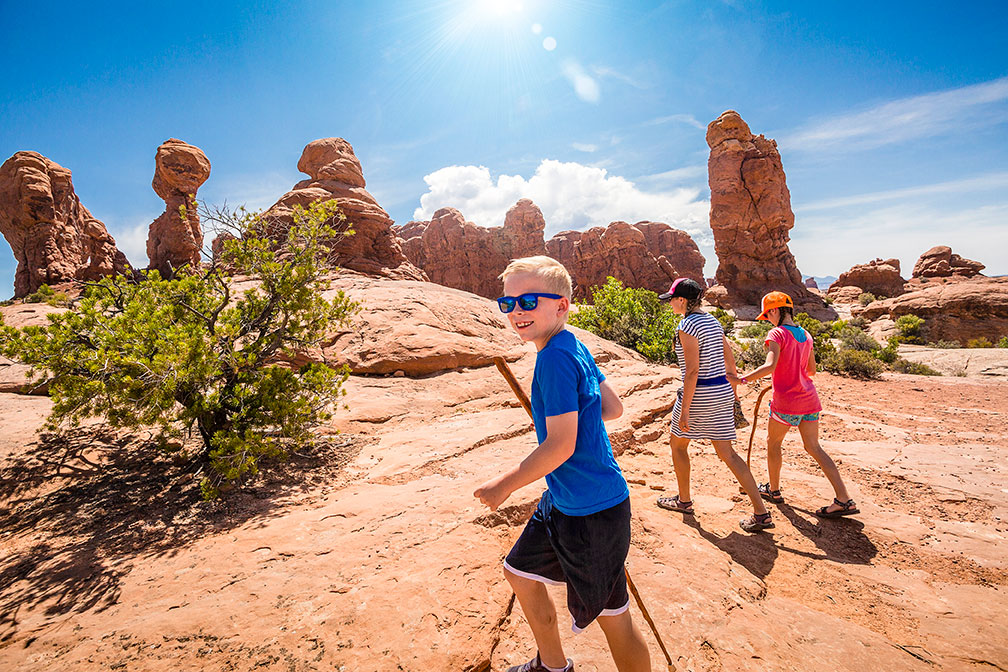 Three people hiking in red rock country with blond boy in foreground.