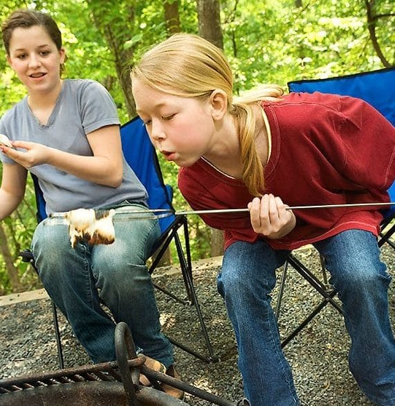 Girl blowing on roasted marshmallow at campfire