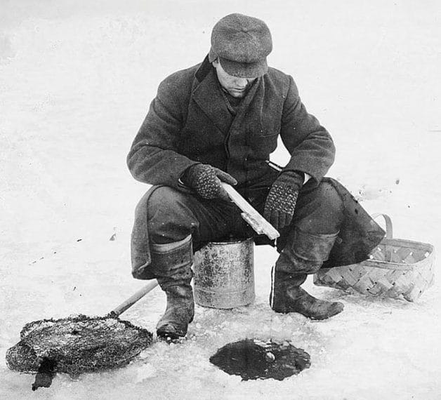 Black and white photo of ice fisherman sitting on bucket