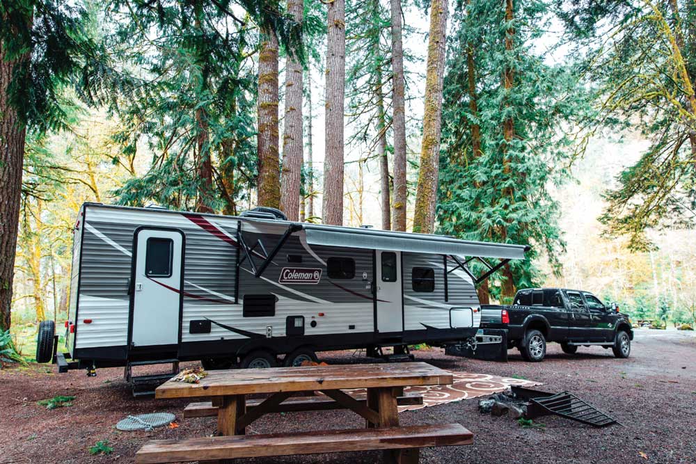 A travel trailer and truck in a forested campsite