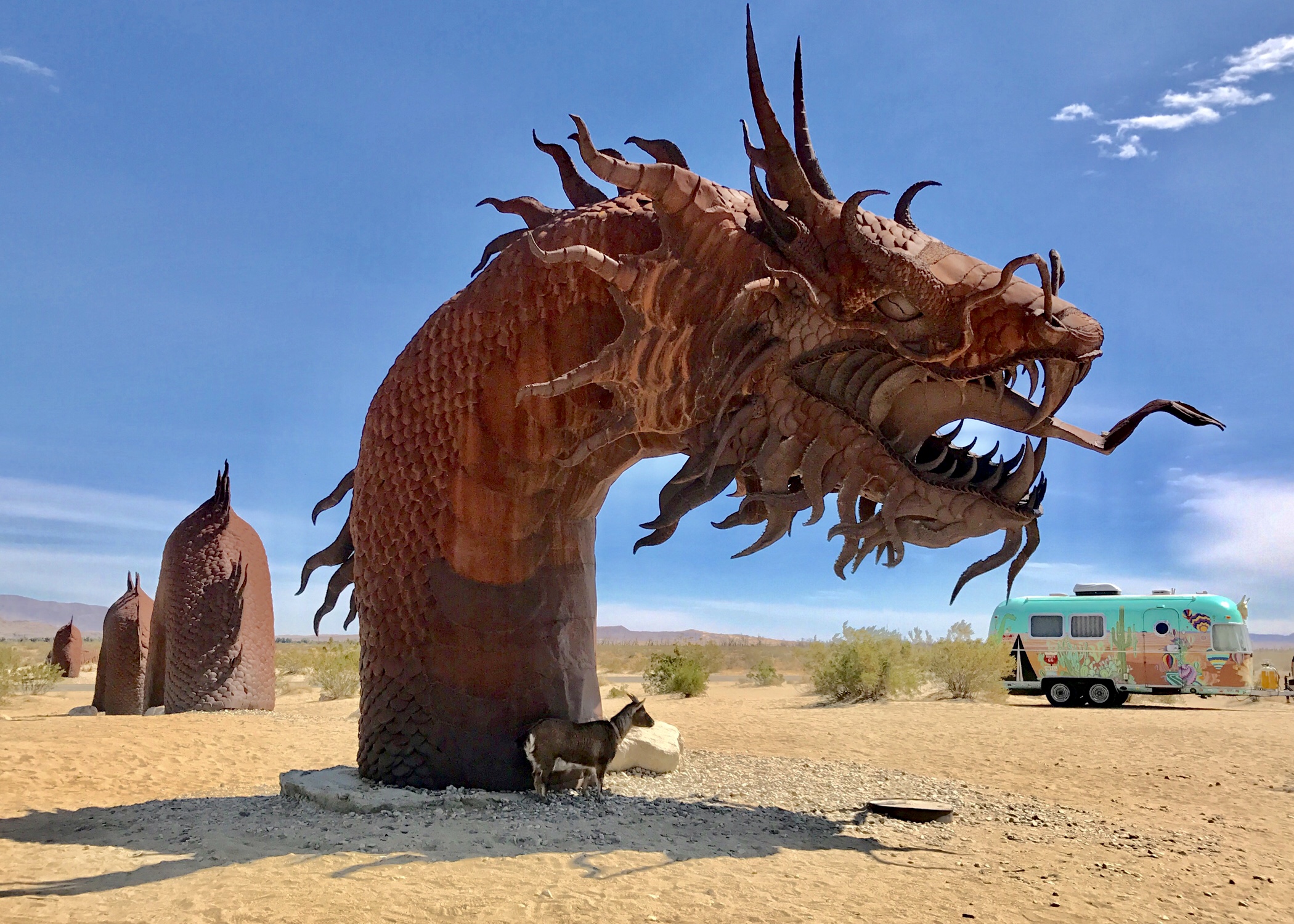 Dragon metal art in Anza Borrego desert with trailer in background and goat in statue's shade