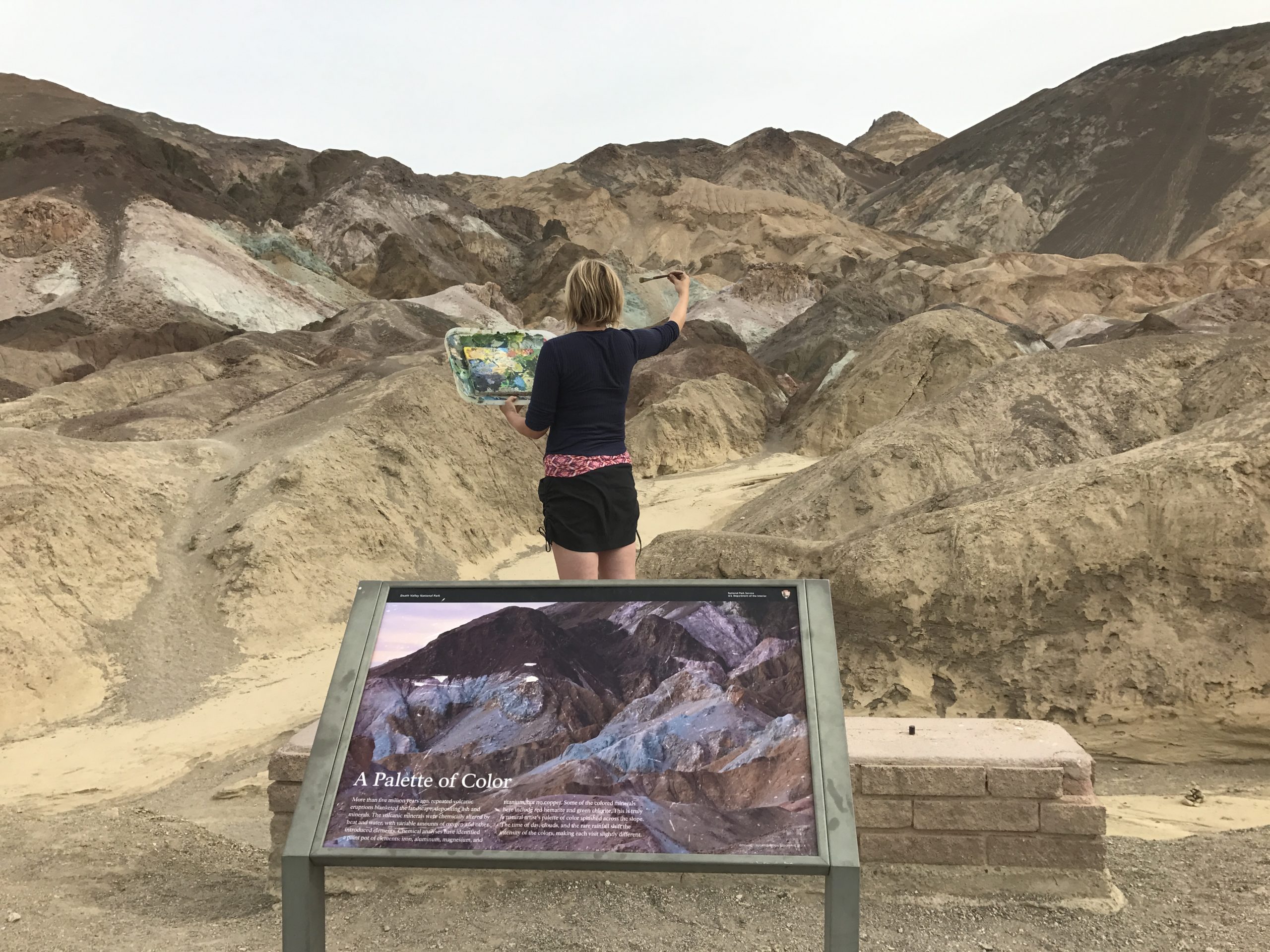 Woman's back looking towards hills holding artists pallet in Death Valley