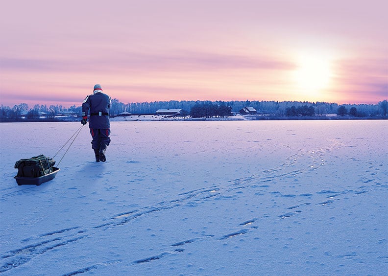 Man walking on frozen lake pulling sled with ice-fishing gear.