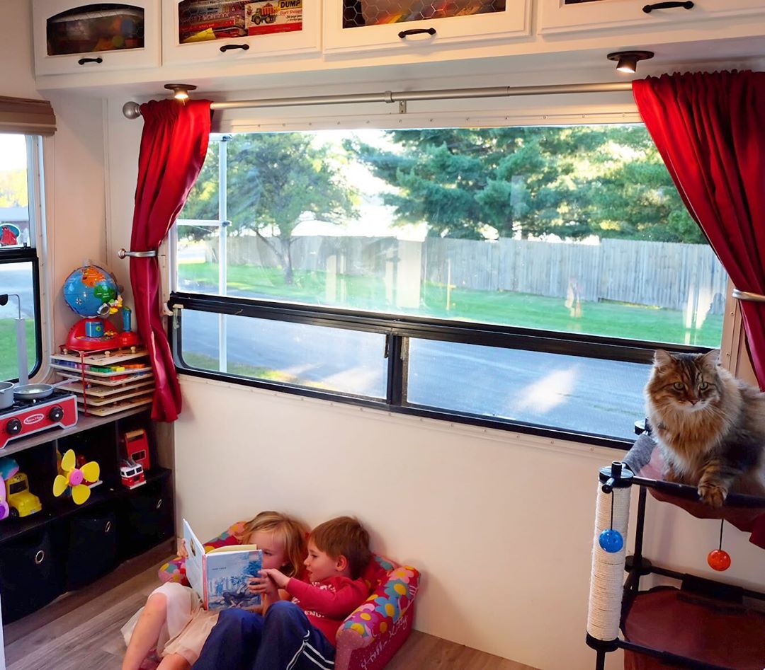 Two toddlers sitting in small couch reading book in trailer