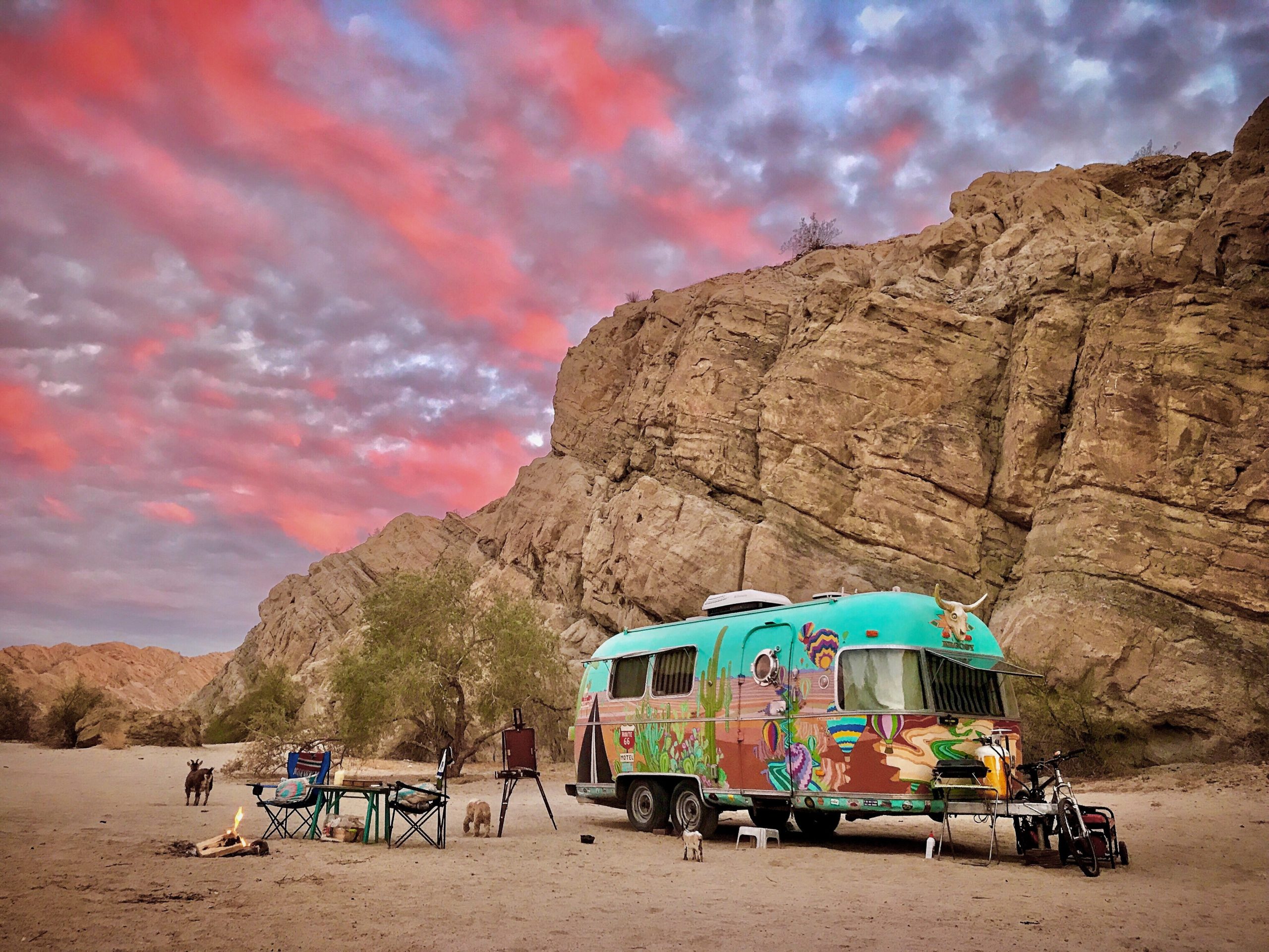 Colorful Airstream trailer parked against Joshua Tree mountain with beautiful pink and purple clouss