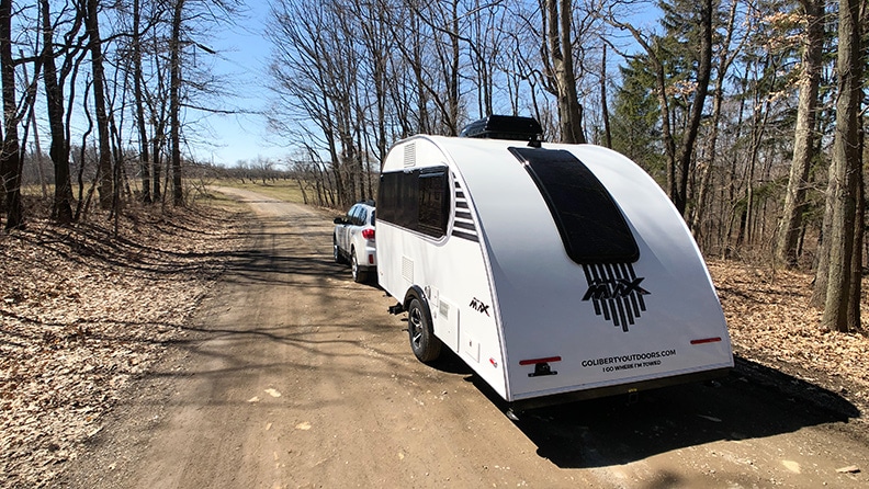 White SUV towing Little Guy Mini Max trailer on tree lined dirt road