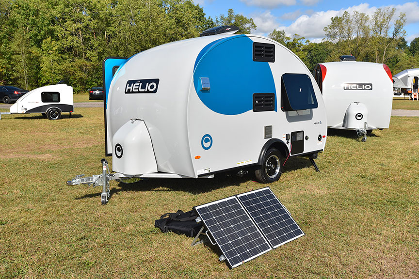 Three small camping trailers on grassy field with solar panel in front.