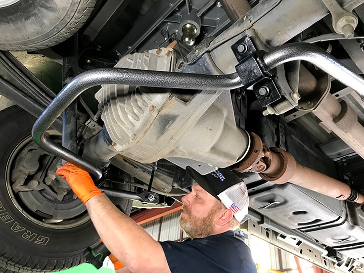 A technician installing Hellwig Big Wig sway bars underneath a Ford F-350.