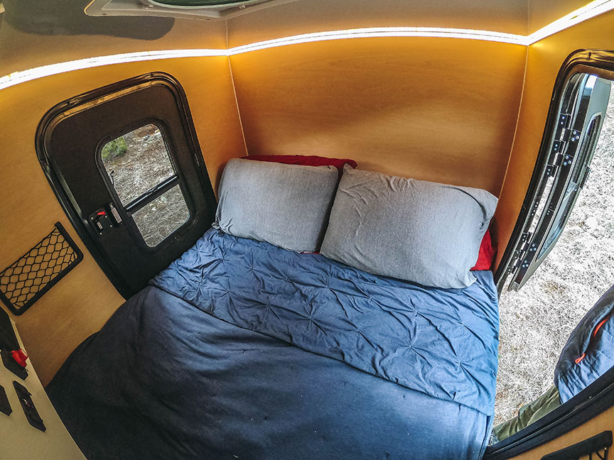 Back of trailer with two pillows on bed and two entry doors.