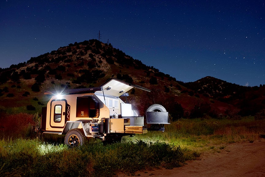 Night scene of trailer with lights on and starry sky above.