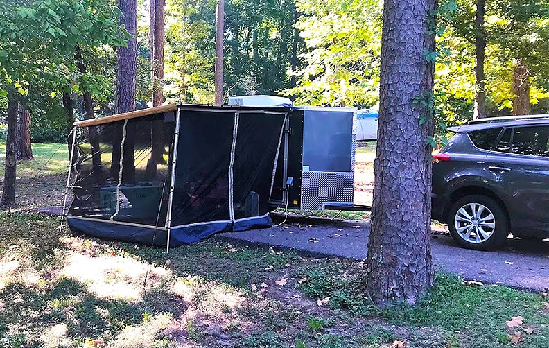 Cargo camp in campsite with screened room on awning and SUV tow vehicle.