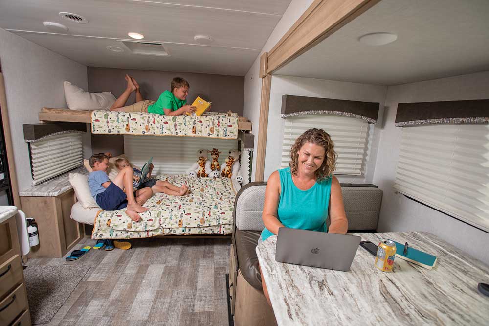 A mom works at the dinette of the Micro Minnie whil the boys read books on the bunks in the background
