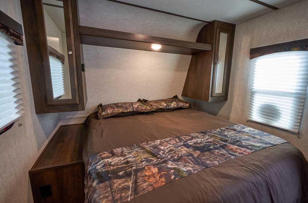 An overhead shelf between the bedroom's wardrobes holds nighttime items. The Mossy Oak Obsession Package includes a nature-inspired bedspread and pillow shams with a leaf-and-tree motif.