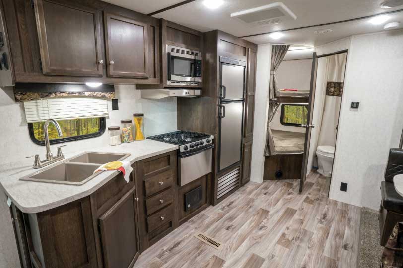 The well-planned kitchen can accommodate multiple chefs; a spacious galley allows occupants to move around freely. Double-over-double bunk beds with Teddy Bear Bunk Mats by Lippert Components are kid-approved. 