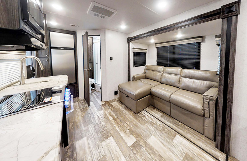 Interior of Super Lite 212FB showing L-shaped sofa and gray vinyl plank floor