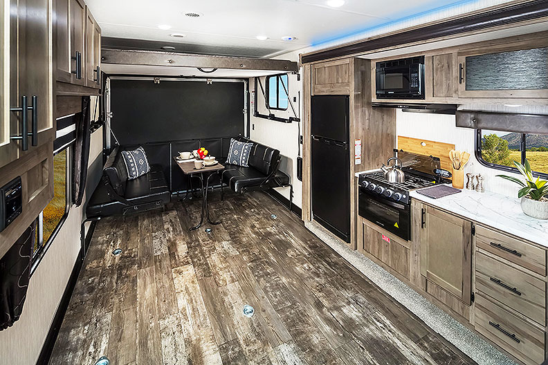 View of toy hauler from midship to rear with plank-look flooring, kitchen and rear sofas.