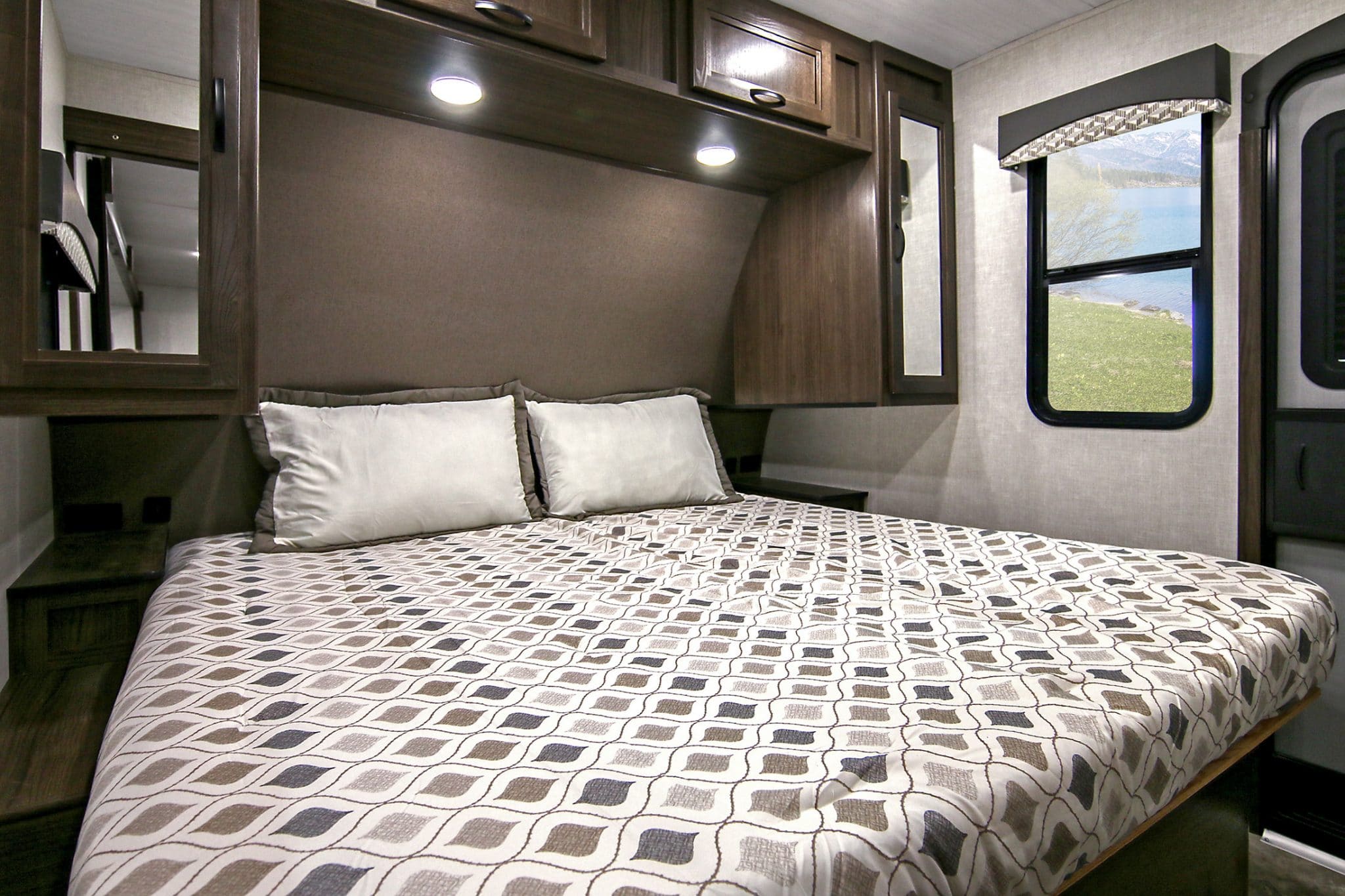 Bed with brown and white bedspread and two pillows in trailer.