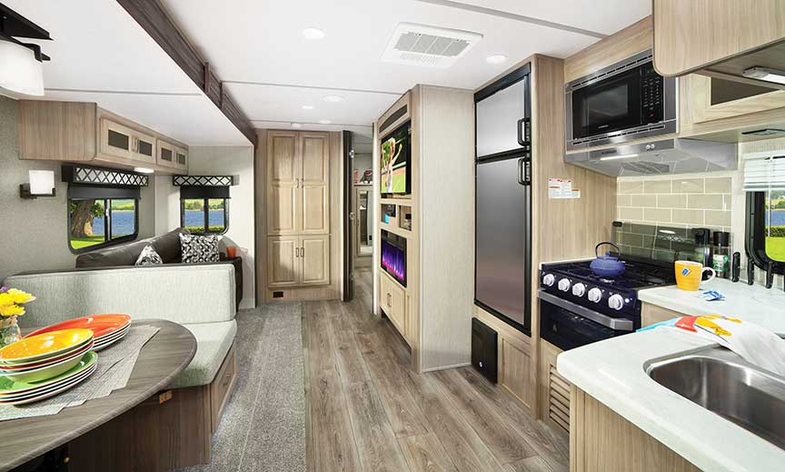 Kitchen in travel trailer with stainless steel double-door refrigerator and white countertops across from dinette.
