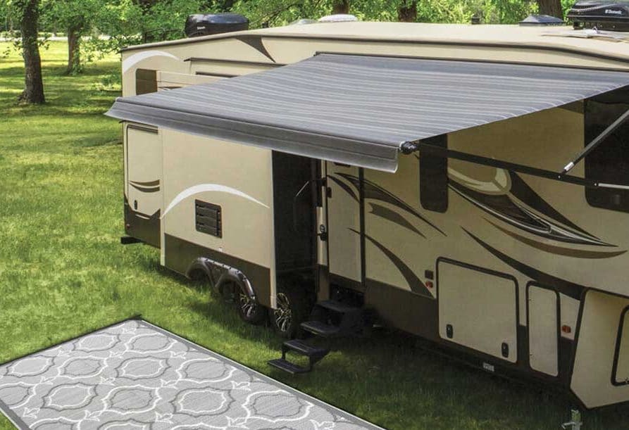 Gray patio mat next to fifth-wheel trailer with awning extended.