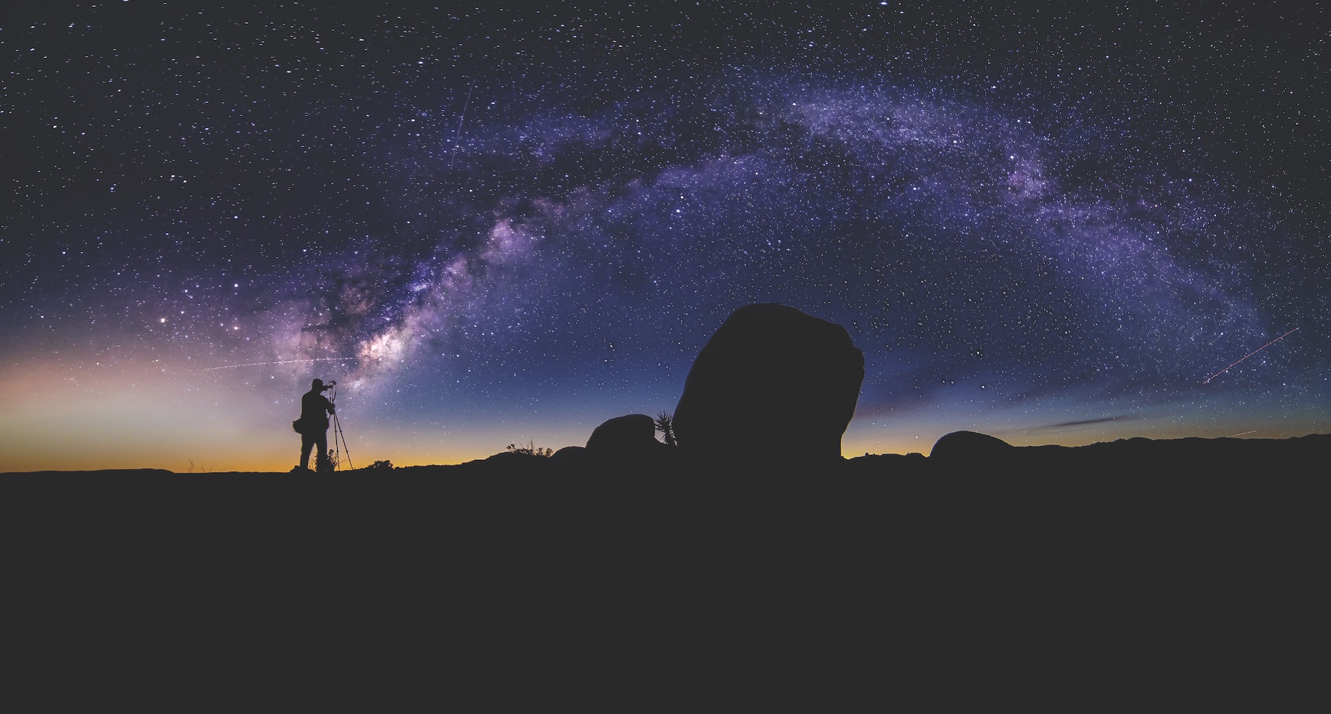 Photographer doing astro photography in a desert nightscape with milky way galaxy. The background is stary celestial bodies in astronomy. The heaven depicts science and the divine.