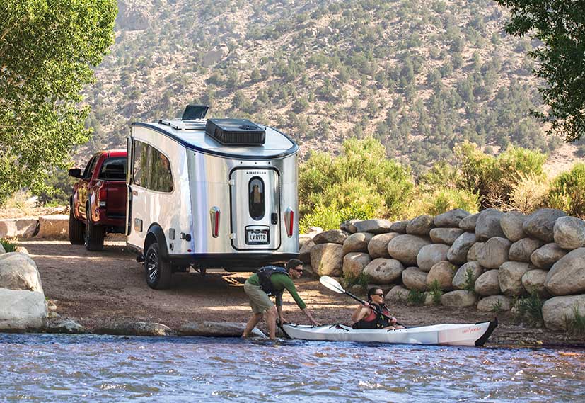 Silver Airstream Basecamp trailer with kayak in foreground.