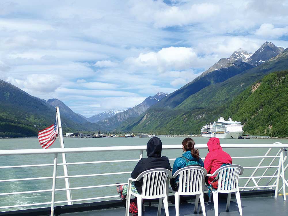 Three people sitting on ferry with cruise ship in sight