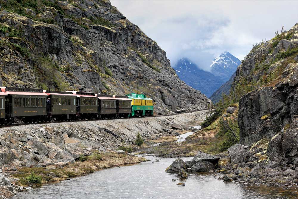 Old train on train track weaving within mountains on cloudy day