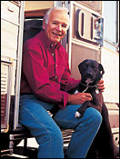 Older man wearing red shirt sitting in RV with dog