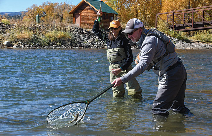 Two fisherman up to knees in Upper Rio Grande River netting a brown trout