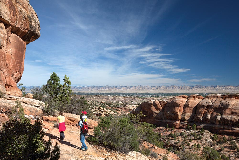 A family hikes to the natural rock room called the Devils Kitchen. In the distance is the town of Grand Junction, located in Colorado’s wine country. 