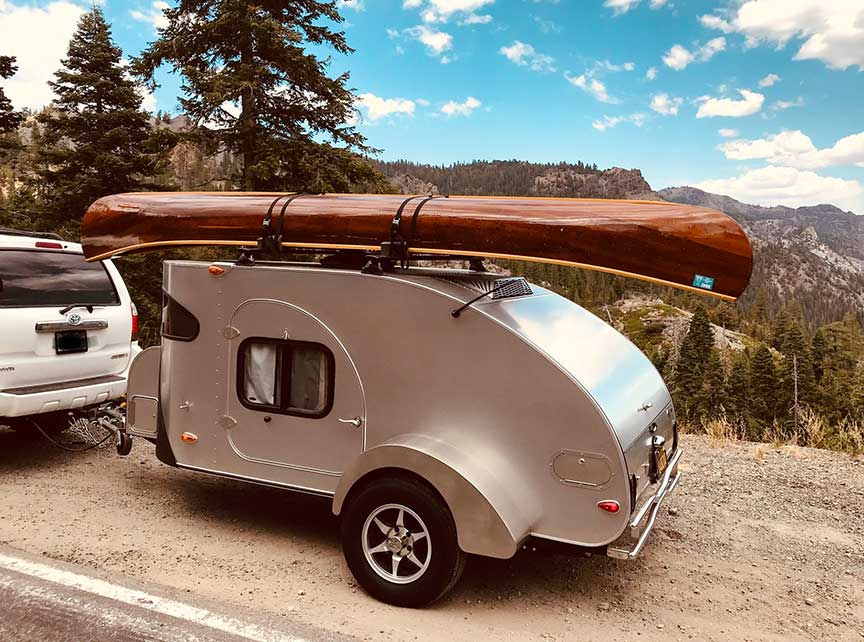 Silver Camp-Inn trailer on road with canoe on top rack.