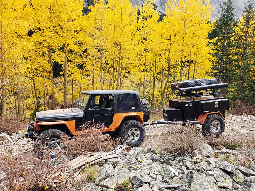 Orange Jeep towing Crawlorado trailer with aspen trees in background.