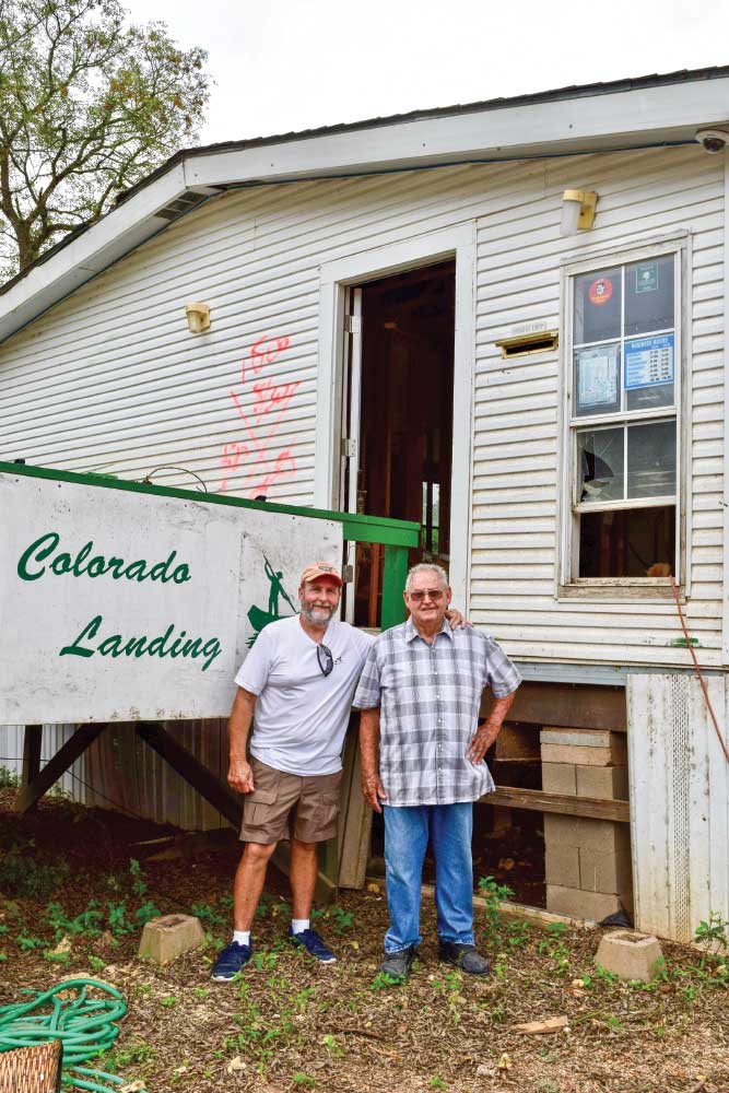 Two older men standing in front of Colorado Landing sign and worn building