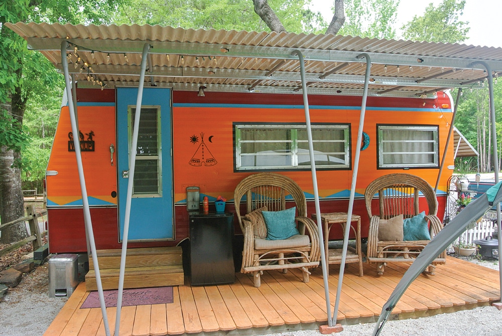 Orange and blue vintage trailer with porch, surrounded by beautiful landscape. 