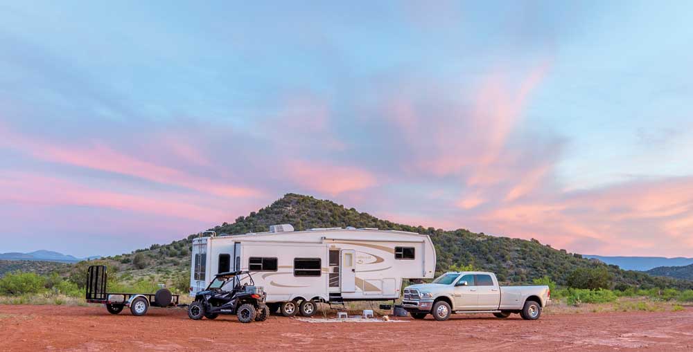 The Fagan's fifth-wheel trailer, truck, Razor side by side and utility trailer are parked under a sunset sky