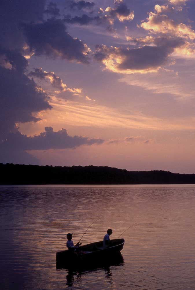 Fishermen in boat on lake at sunset