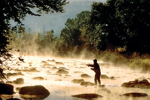 Man fishing, standing within large rocks in stream 