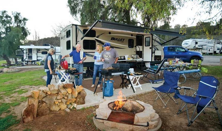 Four people cooking on grills in front of travel trailer