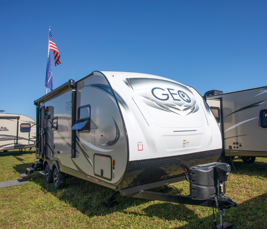 White travel trailer with American flag on top parked in grassy lot