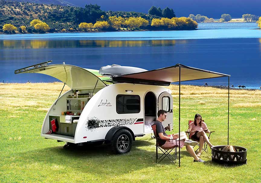 Couple in front of Luna Rover trailer at lakefront campsite.