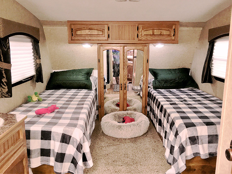 Twin beds in RV with cabinets and closets between them.