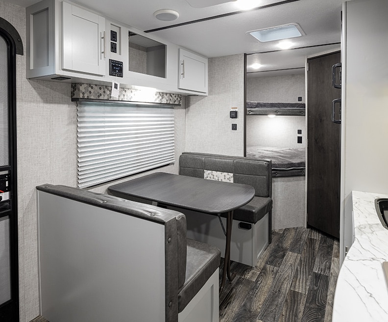 White interior with gray bench dinette and white cabinets above it. Bunks in the rear.