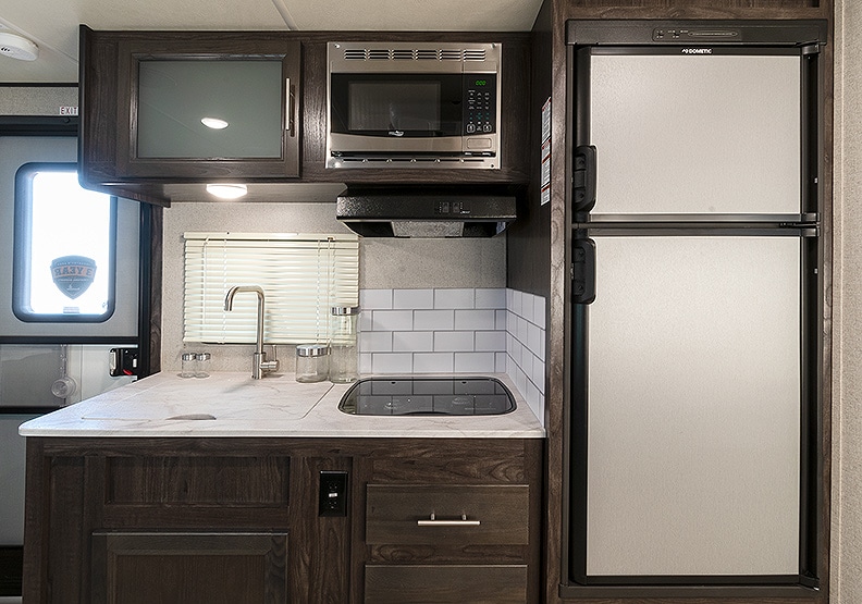 Kitchen with light colored counters, dark wood cabinets, microwave, sink and refrigerator.