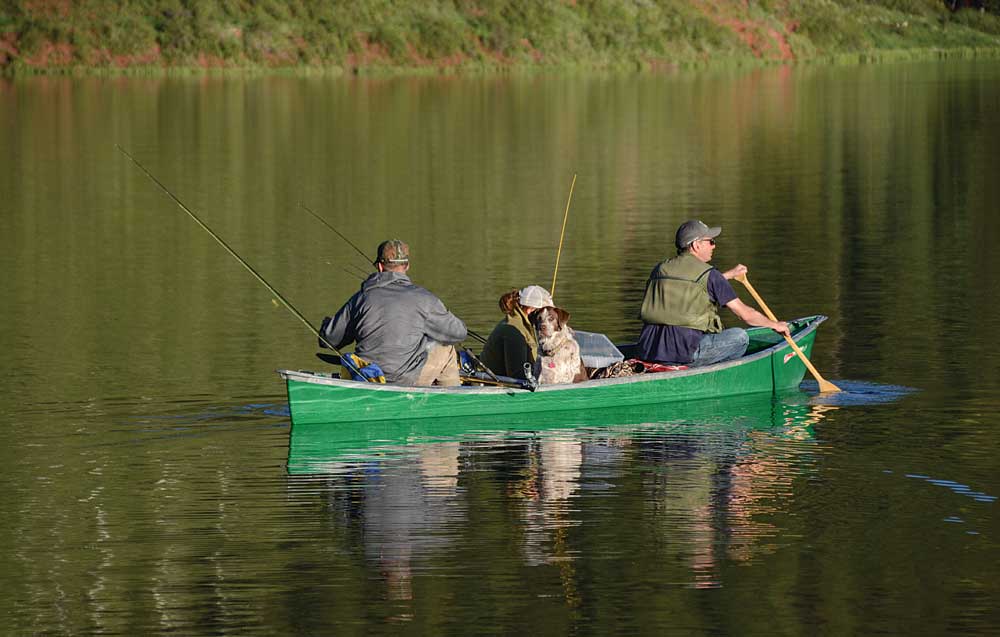 Canoe on a lake loaded with fishermen and a dog