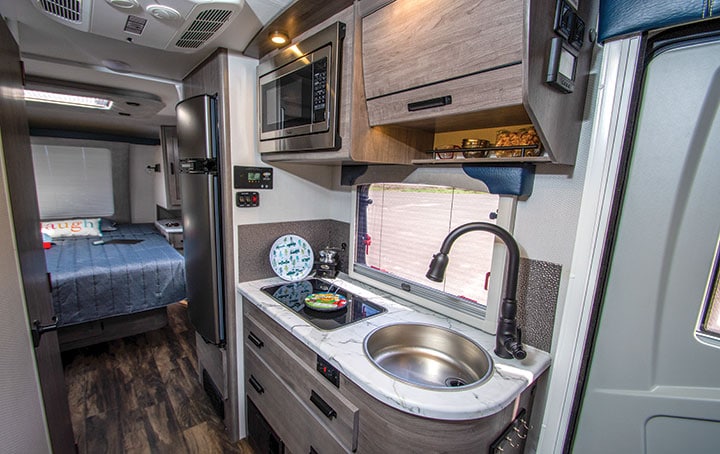 Kitchen with sink, range, cabinets and drawers with bedroom in background in Lance 2075 travel trailer