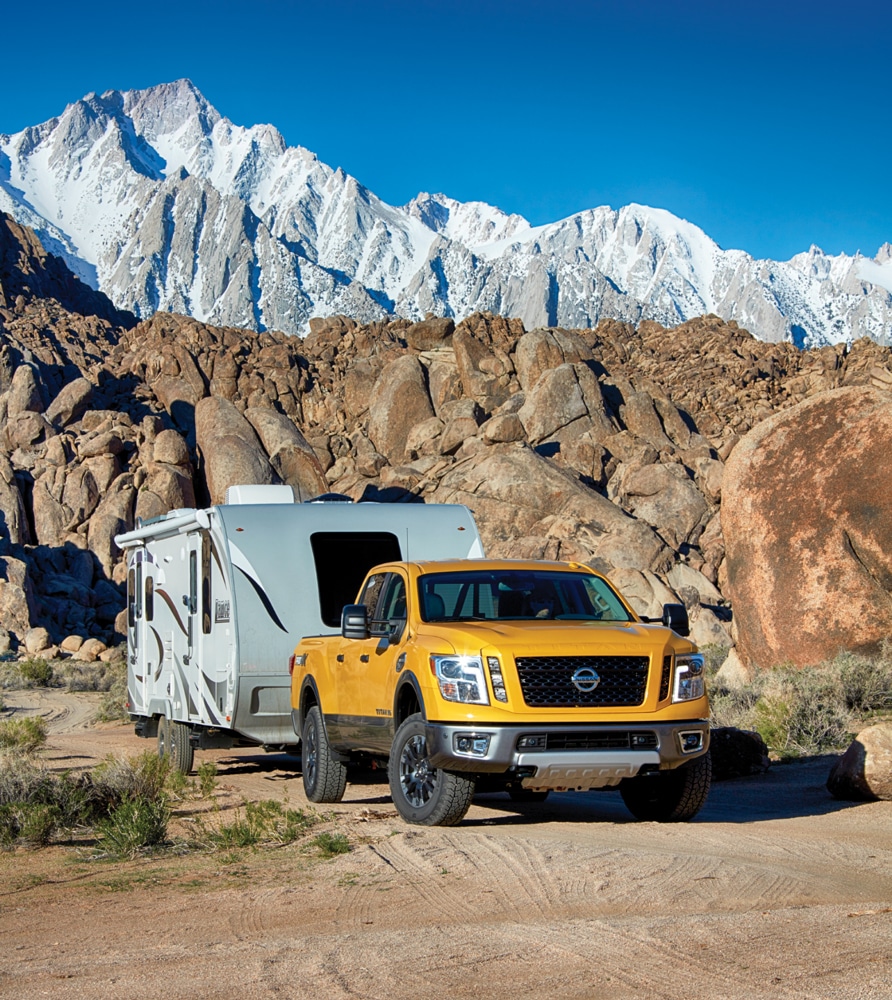 Yellow truck pulling travel trailer with white capped mountain backdrop