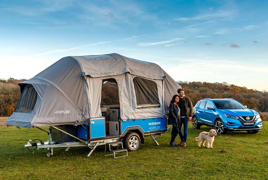 Couple in front of Opus camper dexter to blue Nissan SUV.